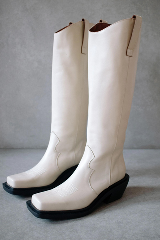A Wild West inspired tall boot featuring classic cowgirl lining and an inverted midi heel.