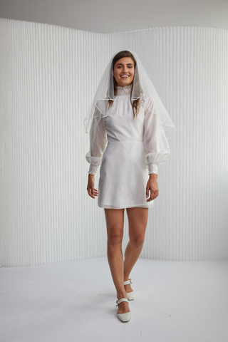 Bold and sophisticated. The Rebecca Dress designed by Vanessa Cocchiaro features the most unique details from its buttoned back, ruffled neck and wrists, and  exaggerated elegant sleeves. Be sure to stand out in this mini length white dress, the perfect number for all of your wedding events.