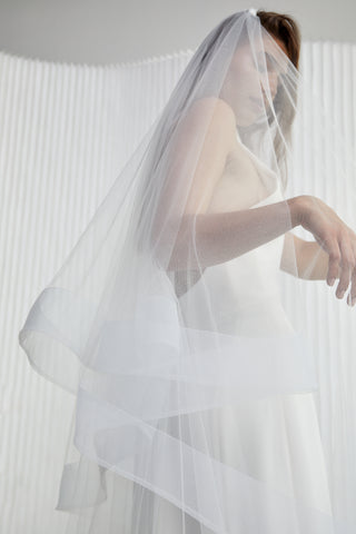 Here's a veil that glows up your bridal look. Hannah is special, she creates a voluminous halo of beauty around you making you radiant amongst your guests. She really is the perfect contemporary statement accessory. Cathedral Length with blusher, metal hair comb. Horse Hair Edge Veil (Sample in White)